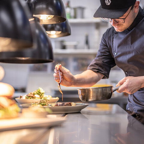 Ein Koch verfeinert das Gericht mit einer aromatischen Soße