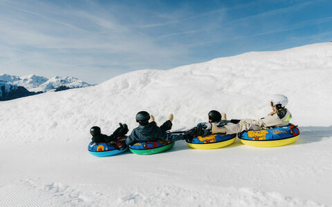 Vier Kinder auf bunten Snowtubing-Reifen in verschneiter Winterlandschaft.