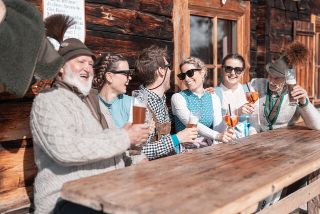 Männer und Frauen genießen Bier und Aperol bei einer Hütte.