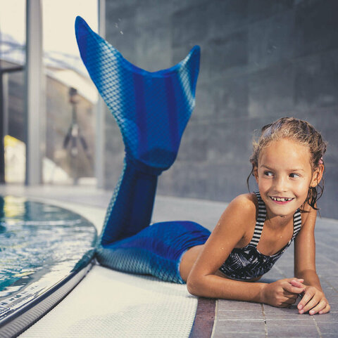 Ein kleines Mädchen mit einer Meerjungfrauenflosse im Kristallbad