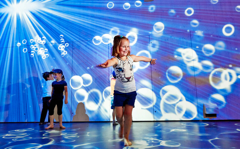 Kinder spielen in einem Raum, in dem Lichter und Luftblasen projiziert werden