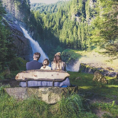 Ein Mann, eine Frau und ein Mädchen sitzen auf einer Bank und beobachten einen Wasserfall