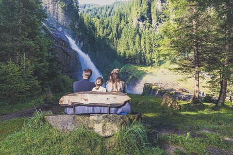 Ein Mann, eine Frau und ein Mädchen sitzen auf einer Bank und beobachten einen Wasserfall