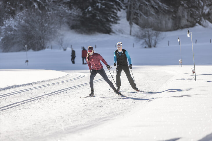Zwei Langläufer auf einer verschneiten, sonnigen Strecke