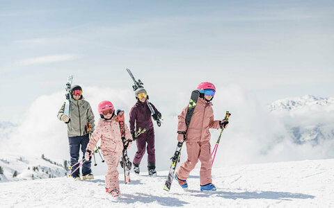 Zwei Erwachsene und zwei Kinder tragen Skier über eine verschneite Berglandschaft.Zwei Erwachsene und zwei Kinder tragen Skier über eine verschneite Berglandschaft.