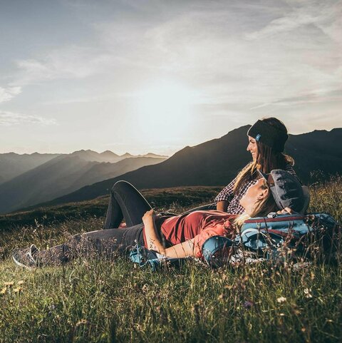 Zwei Frauen liegen in einer Wiese und blicken auf eine traumhafte Bergkulisse