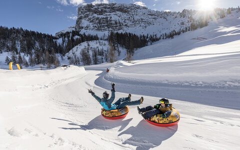 Zwei Personen fahren auf luftgefüllten Reifen die Piste hinunter