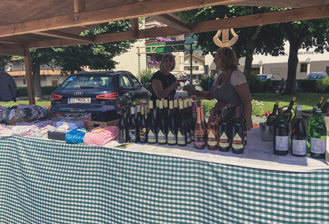 Zwei Frauen stoßen beim Bauernmarkt mit einem Glas Wein an