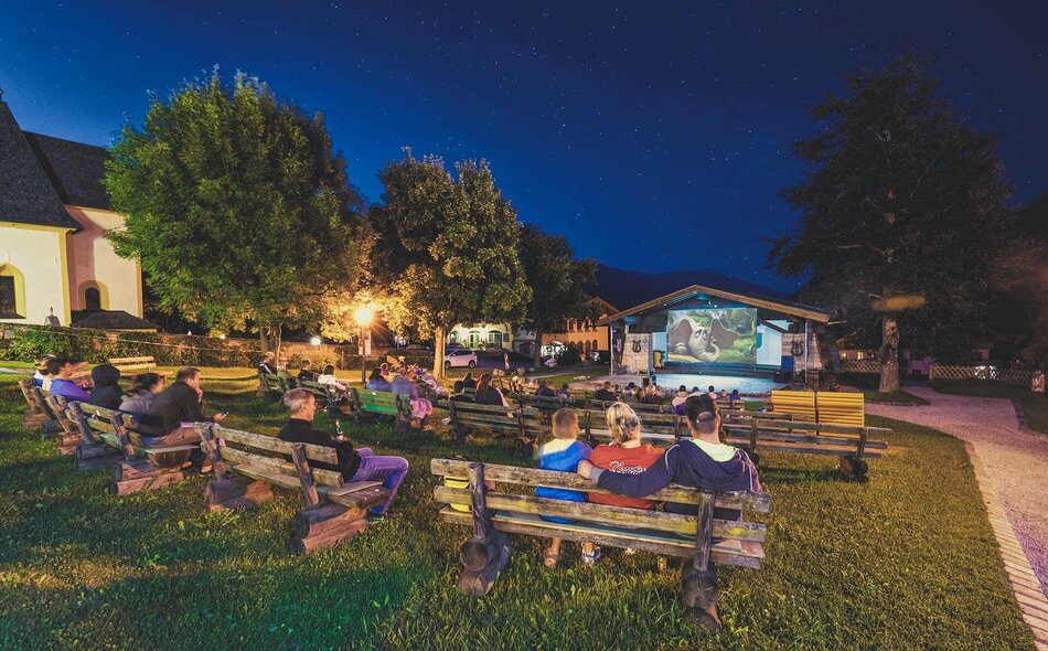 Zuschauer sitzen auf Holzbänken beim Fallkino Krimml