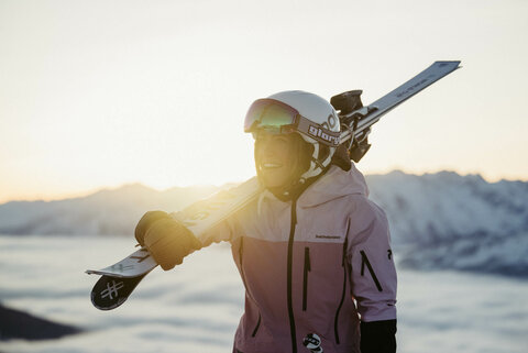 Eine Skifahrerin mit Skiern auf den Schultern vor dem Sonnenaufgang