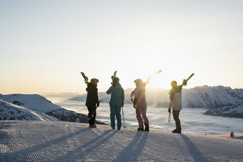 Vier Leute mit den Skiern auf den Schultern schauen in den Sonnenaufgang