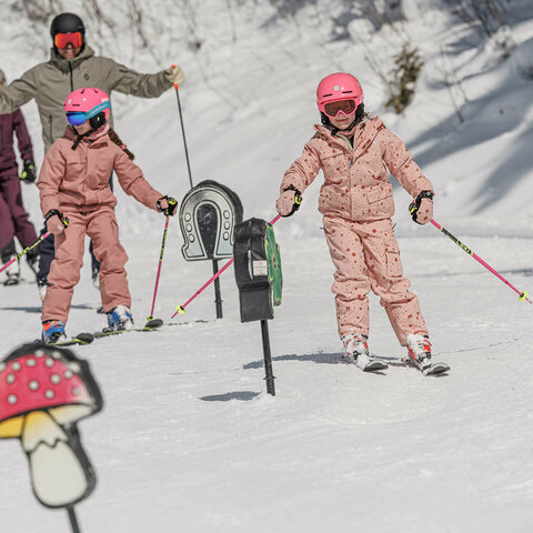 Eine Familie fäührt mit Skiern an Hindernissen auf einer verschneiten Skipiste vorbei.