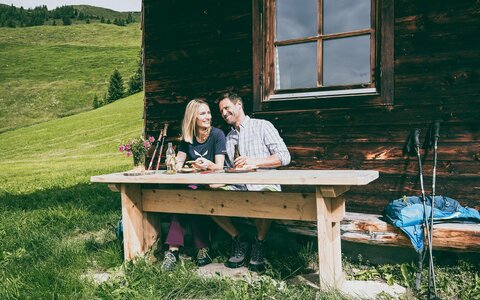Ein Mann und eine Frau essen eine Brotjause bei einer Hütte