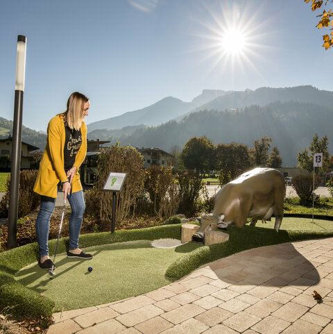 Frau spielt Minigolf, dahinter eine Bergkulisse