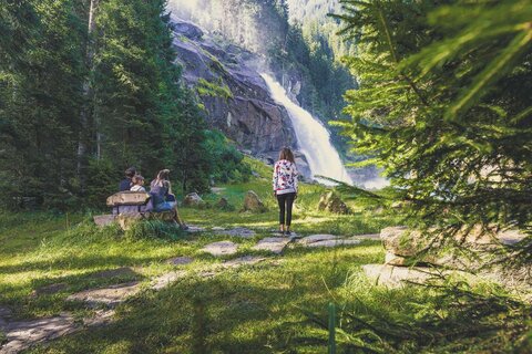 Ein Mann, eine Frau und ein Mädchen sitzen auf einer Bank und beobachten einen Wasserfall