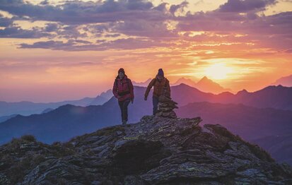 Ein Mann und eine Frau wandern am Kreuzjoch, mit traumhaften Sonnenaufgang im Hintergrund