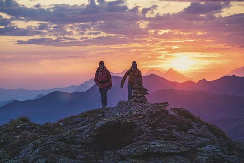 Ein Mann und eine Frau wandern am Kreuzjoch, mit traumhaften Sonnenaufgang im Hintergrund