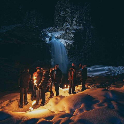 Personen stehen bei einer Fackelwanderung vor einem Wasserfall