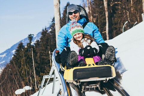 Vater und Tochter fahren mit der Winterrodelbahn