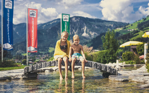 Ein kleiner Junge und ein Mädchen sitzen am Teich vor dem Kristallbad