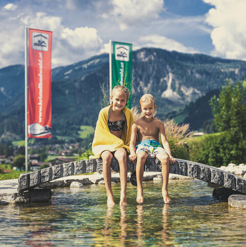 Ein kleiner Junge und ein Mädchen sitzen am Teich vor dem Kristallbad