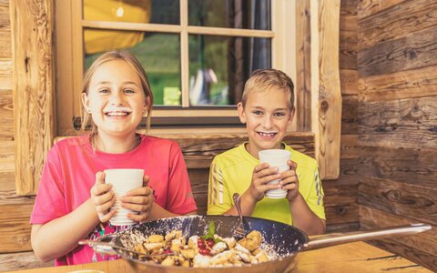 Ein Junge und ein Mädchen sitzen vor einem Kaiserschmarrn und trinken ein Glas Milch