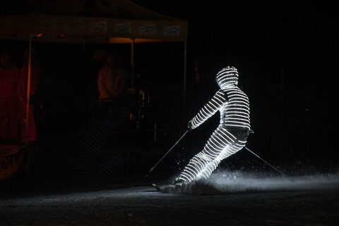 Ein Skifahrer ist von Kopf bis Fuß beleuchtet und fährt im Dunkeln die Piste herunter