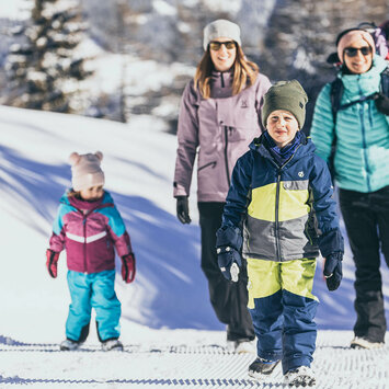 Zwei Frauen und drei Kinder spazieren im Schnee