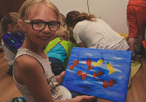 Ein Mädchen zeigt ein selbstgemaltes Bild mit Fischen darauf