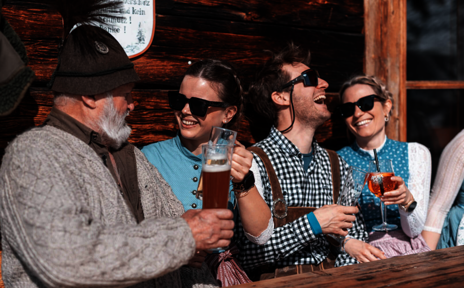 Frauen und Männer in Tracht trinken an einer Hütte.