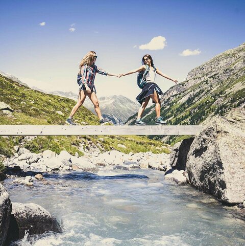 Zwei Frauen gehen händchenhaltend über eine Holzbrücke